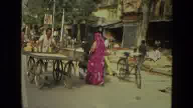 India (1974): Driving Along A Busy Street In India Where Merchants Are Selling