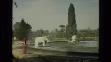 India (1974): People Walk Through An Arboretum With A Pond And Garden Of Flowers