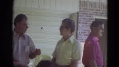 Lincoln Nebraska (1974): A Man Passes By People Standing And Shakes Another Man's