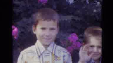 Lincoln Nebraska (1974): Two Boys Smile And Wave In Front Of A Beautiful Bush