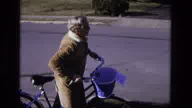 California USA (1975): Elderly Lady Sits On Bicycle On The Sidewalk With Basket