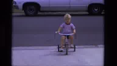 California USA (1975): A Young Boy Rides A Tricycle Slowly Accelerating Along The