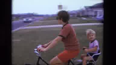 California USA (1975): Boy Rides His Little Brother On A Bicycle Through His