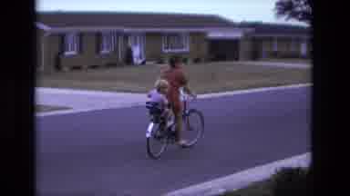 California USA (1975): A Woman Rides A Bicycle Through A Suburban Street With A