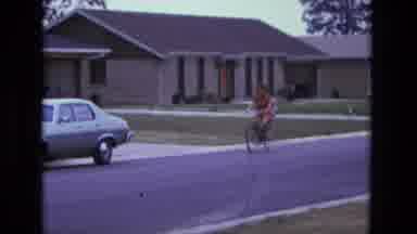 California USA (1975): Woman Slowly Riding A Bike With A Young Baby In A Seat On
