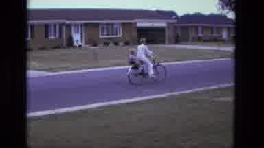 California USA (1975): Woman Riding A Bicycle With A Child In A Child Seat