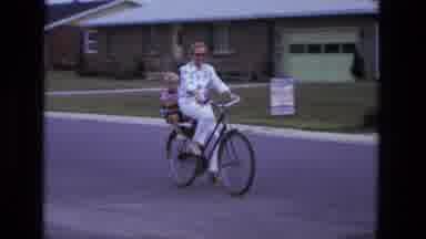 California USA (1975): Woman Rides A Bicycle In The Street With A Child In The