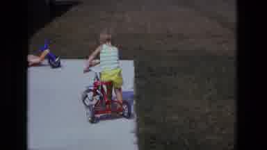 California USA (1975): A Kid Trying To Learn To Ride A Tricycle As He Is Looking