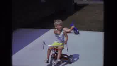 California USA (1975): Little Boy Rides Tricycle And Is Pushed On A Swing