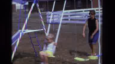 California USA (1975): Woman Wearing Sunglasses Pushes Child On Swing Set In Yard