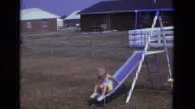 California USA (1975): Blonde Child In Bright Yellow Shorts Slides Down A Slides