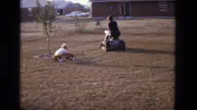 California USA (1975): Person On A Lawn Mower Pulling A Child Around In Wagon In