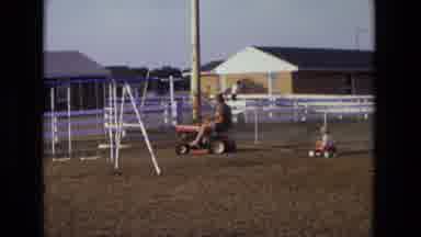 California USA (1975): Father Driving Tractor Pulling Daughter In Wheelbarrow