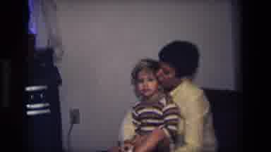 California USA (1975): Woman Putting A Child's Socks On While The Child Waves And