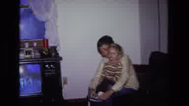 California USA (1975): Mother Sits On The Couch With Baby In Her Lap And Both And