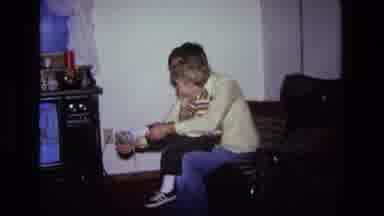 California USA (1975): Mom Sitting On Couch In Front Of Television Putting Shoes