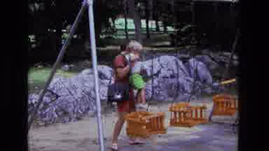 California USA (1975): A Women Putting A Child Inside A Swing While On Vacation