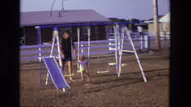 California USA (1975): Father Playing With Child In Backyard Swinging On Swing Set