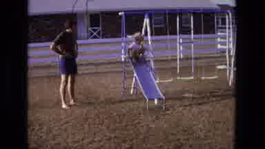 California USA (1975): A Child Is Going Down A Slide On A Backyard Swing Set As