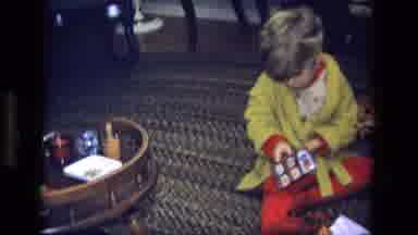 California USA (1975): Little Boy In Yellow Robe Tries To Open The Package And