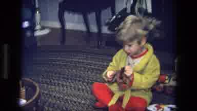 California USA (1975): Boy Wearing Yellow Robe Sits On Floor Opening Christmas