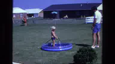 California USA (1975): Little Blonde Haired Boy Filling Up A Blue Blow Up Pool