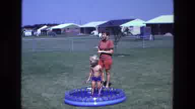 California USA (1975): Little Boy Using A Garden Hose To Fill His Small Blue Blow