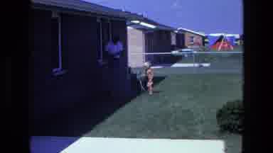 California USA (1975): A Young Boy Cranks A Hose In The Front Yard Of A House Next