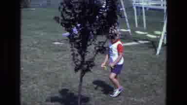 California USA (1975): Child Walking On A Backyard Past A Swing Set Going Into