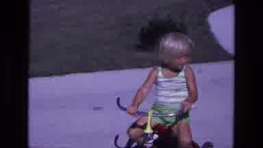 California USA (1975): Little Boy Races Around The Driveway On His Tricycle On A