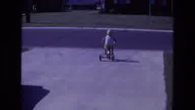 California USA (1975): Child Riding Tricycle Down Driveway Turning Right To Go Up