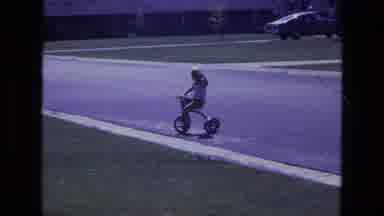 California USA (1975): Child On Tricycle Waving As He Pedals Away While Another
