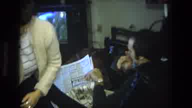 California USA (1975): Man Reading Newspaper While Woman Stands Up And Child Looks