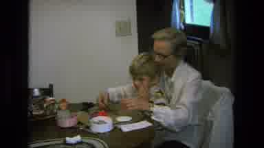 California USA (1975): Boy Sitting With Older Woman At Kitchen Table And Playing