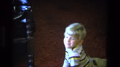 California USA (1975): Boy Wearing Yellow Pants Sits On Brown Floor Watching