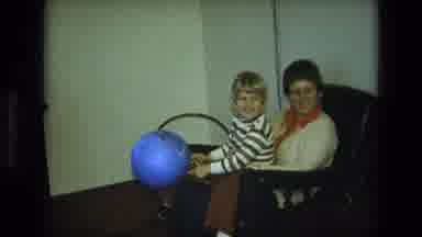 California USA (1975): Lady Sitting In Chair In Living Room While Little Boy Plays