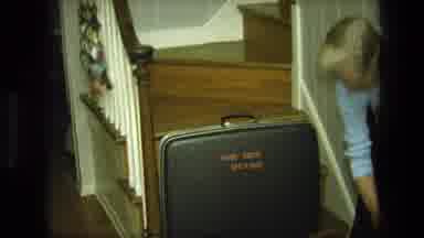 California USA-1975: Woman Picking Up Suitcase At Bottom Of Staircase