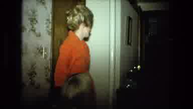 Fort Wayne Indiana (1976): People Gather In Dark Room Around A Table And Chairs
