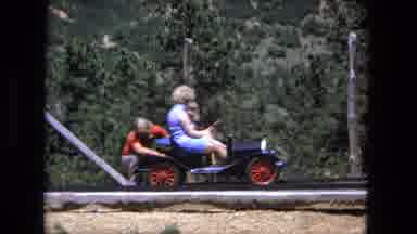 Fort Wayne Indiana (1976): Woman And Child On Old Time Toy Car Driving Along A