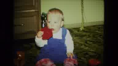 Fort Wayne Indiana (1976): Baby Wearing Blue Overalls Puts Red Object Into Mouth