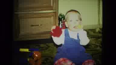 Fort Wayne Indiana (1976): Baby Wearing Blue Overalls Puts Yellow Object Into