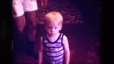 Fort Wayne Indiana (1976): Person Wearing White Shorts Picks Up Boy Wearing Blue