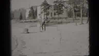 New York City (1956): Black Dog Walks Past Man Wearing Black Pants On A Sunny Day
