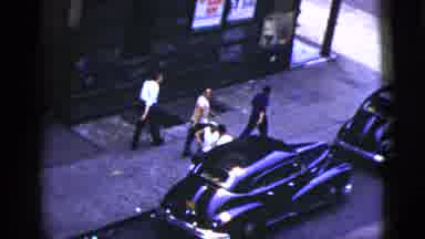 New York City (1956): Three Men Walking Through City Street Whilst People Watch On