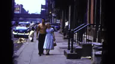 New York City (1956): A Lady In A Dress And Man Without A Shirt Walk Down A City