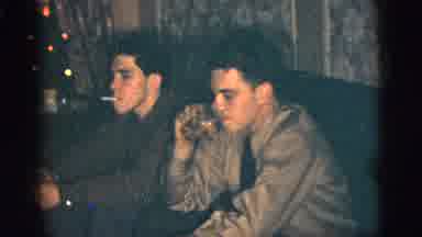 New York City (1956): Man Wearing Black Suit Talks To Two Men Sitting On Sofa