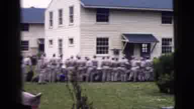 New York City (1958): Crowd Dressed In Grey Uniforms Stands Next To White Building