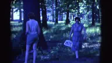 Clarkdale Arizona (1961): Woman With Dustpan Walks Past Another Woman In The Woods