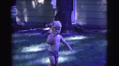 Clarkdale Arizona (1961): Young Boy In Swim Trunks Wonders In Yard As He Sucks His