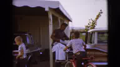 Clarksdale Arizona (1968): People Unload Clothes From Brown Car On A Clear Day